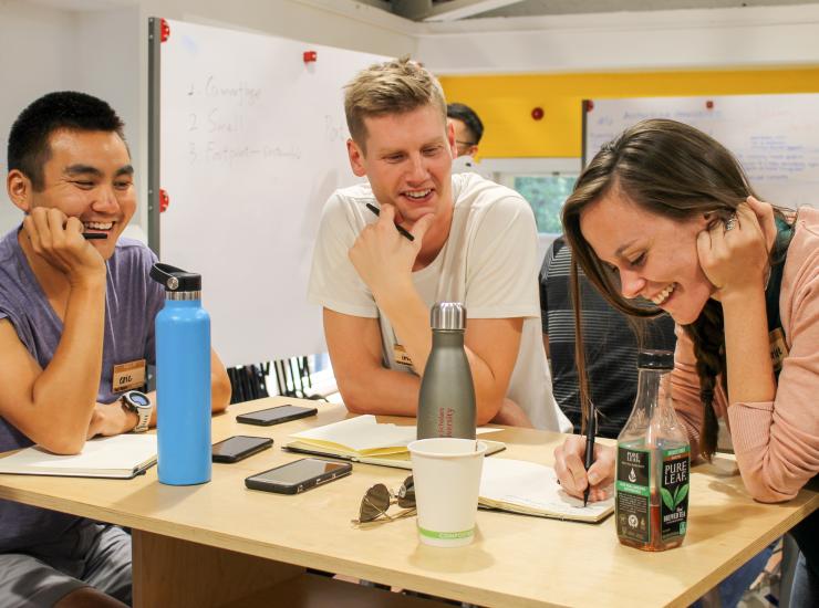 Three participants around a desk smiling at their notes.