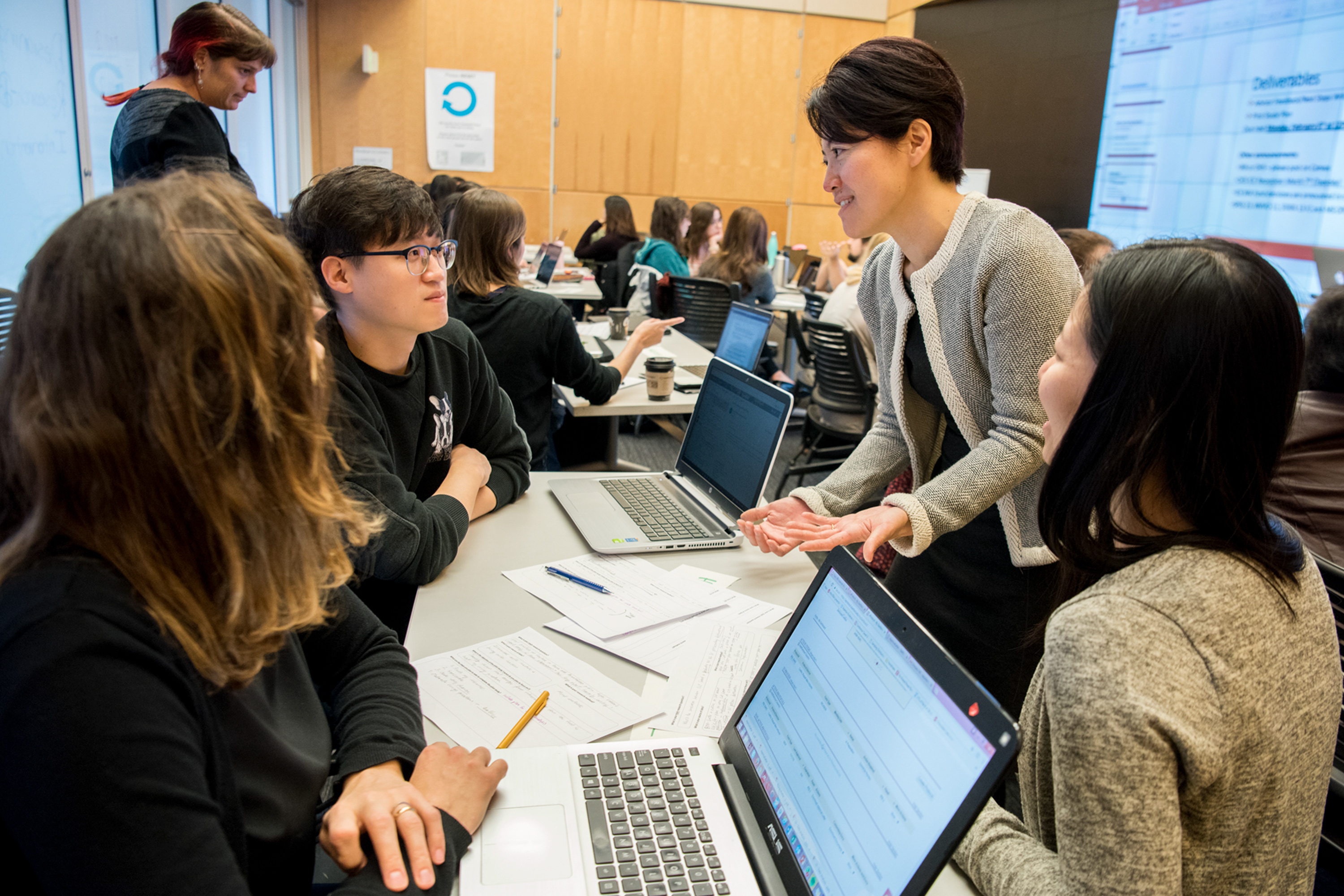 A female teacher talking with three students at a table.