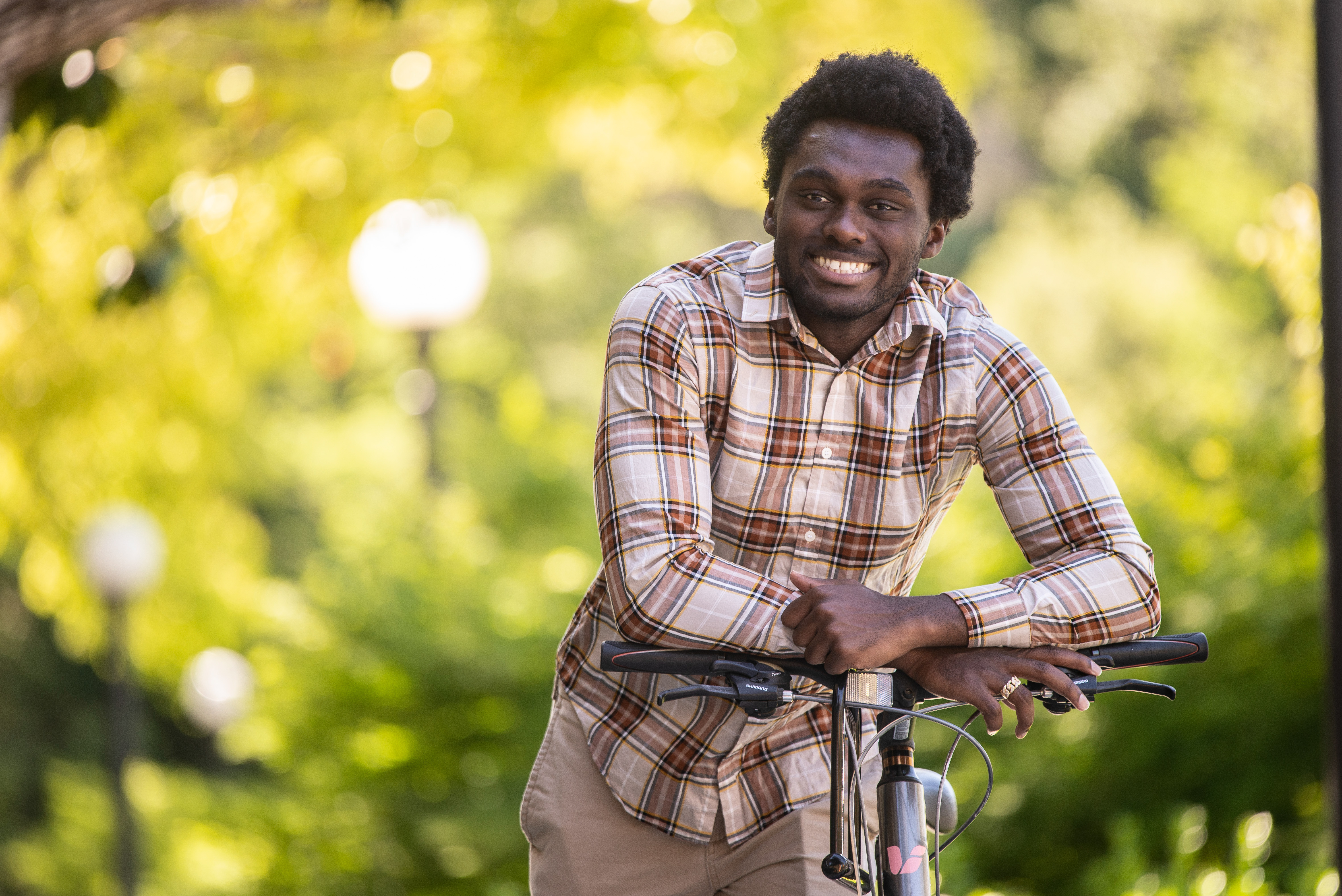 Photo of Cordy McJunkins, leaning on his bike handlebar with lush greenery behind 