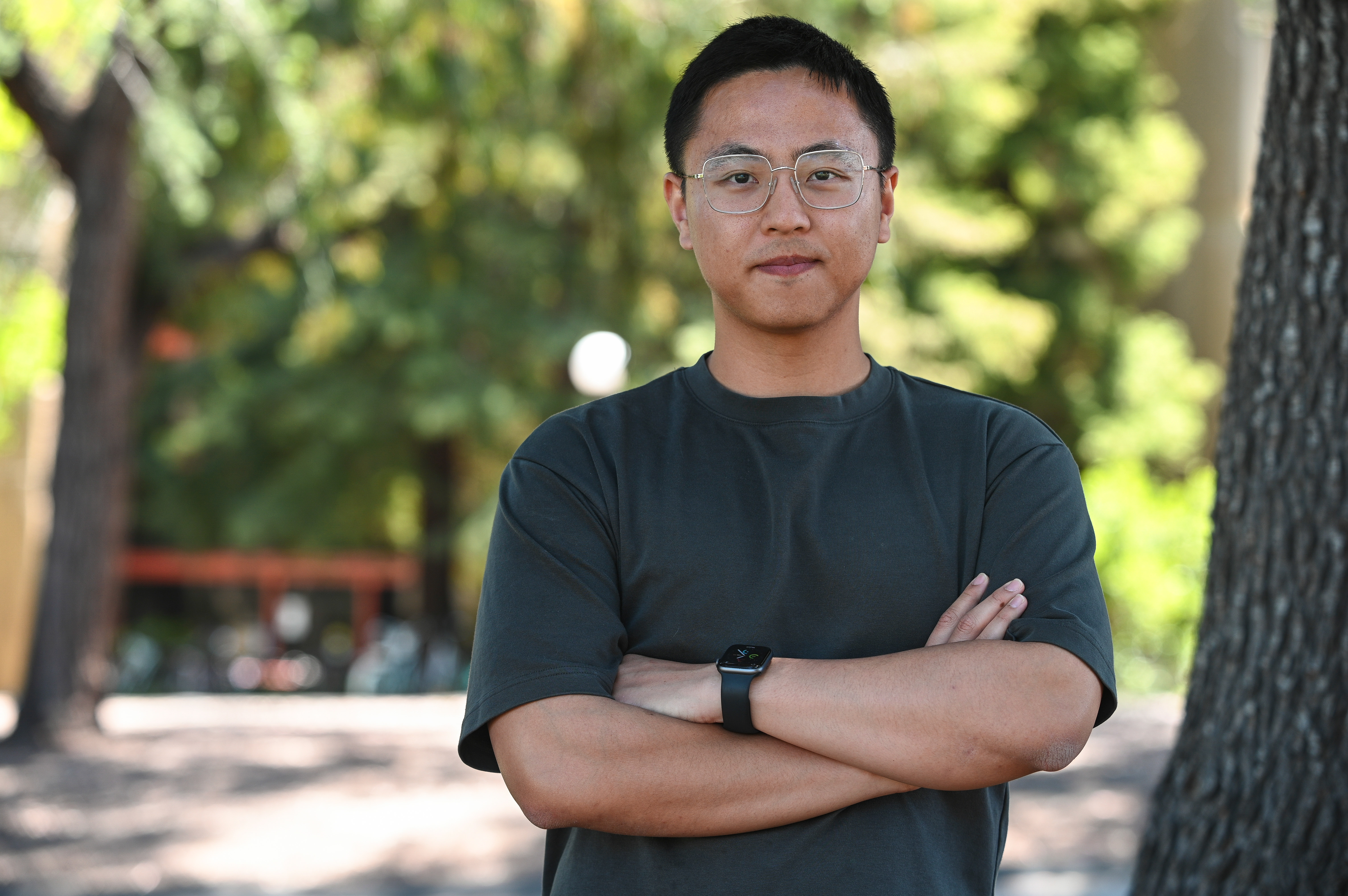 Photo of Richard Tang, standing with arms folded, in front of sunny greenery