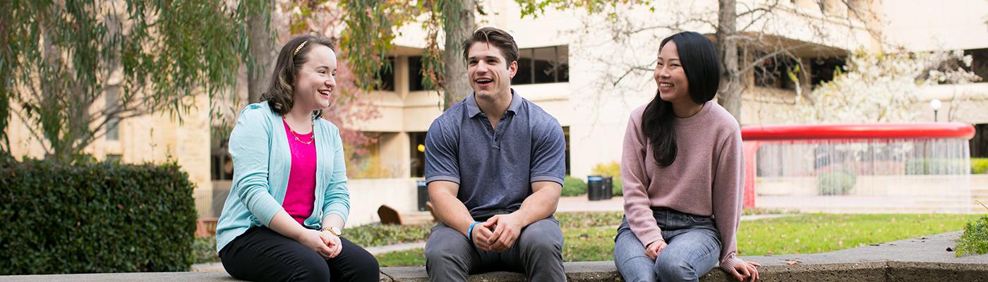 Three students sitting and talking in front of library.