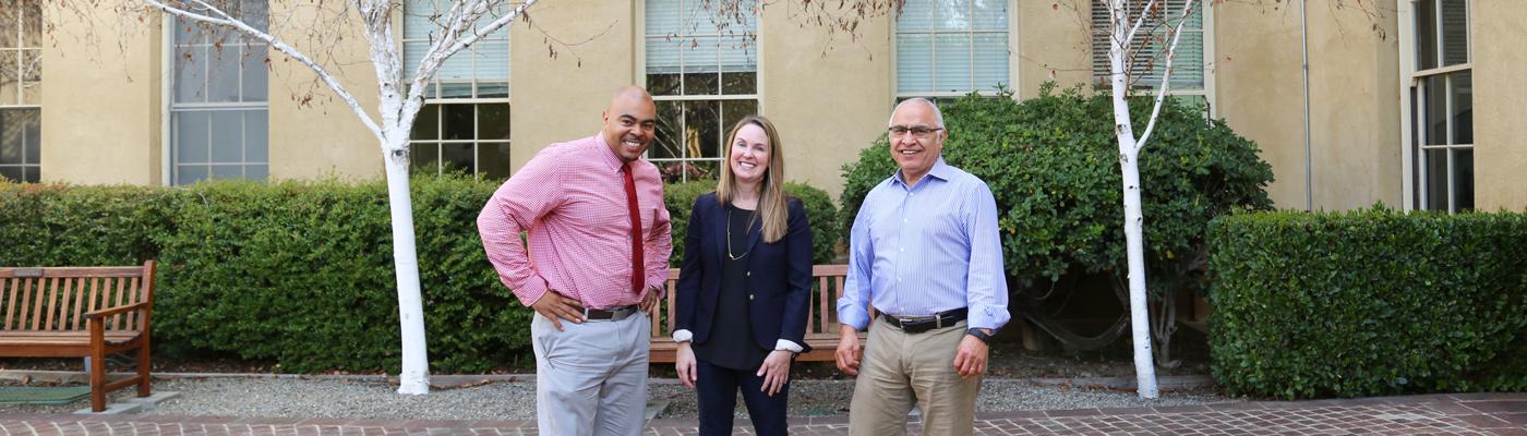 Three faculty members standing in front of school building.