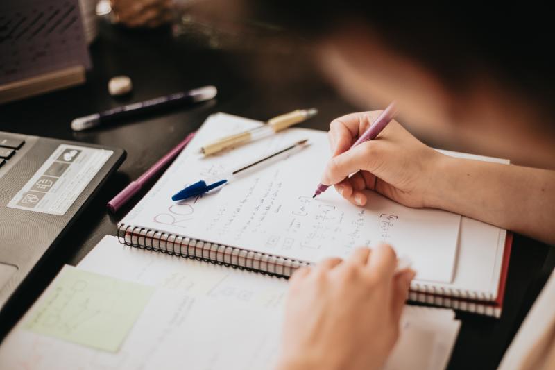 Close up detail image of a young woman studying and working on her home desk doing homework during university