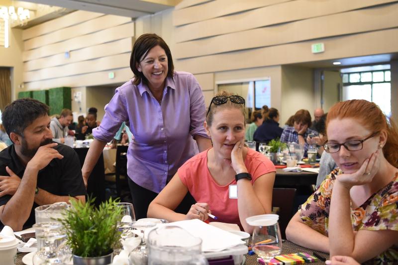 Jo Boaler standing with a table of participants at a workshop.