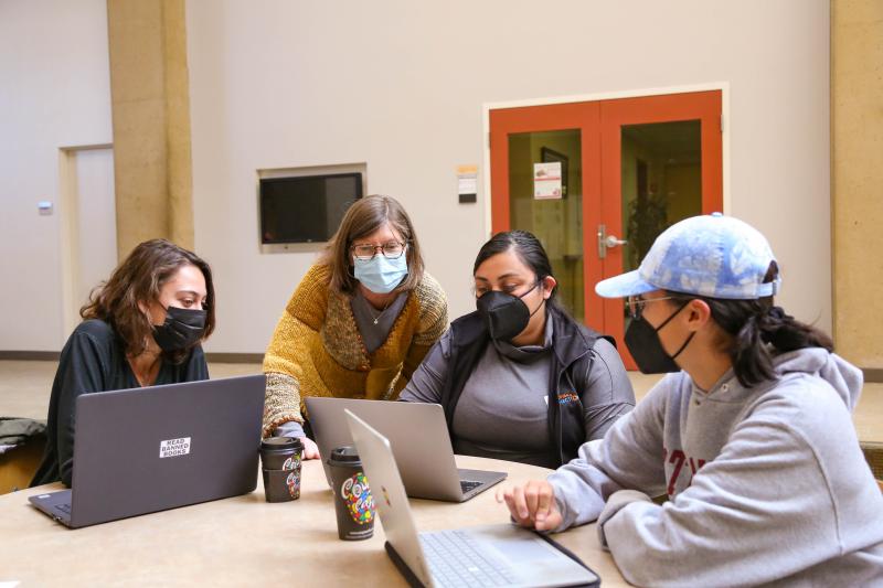 Teacher and students around a table looking at a laptop