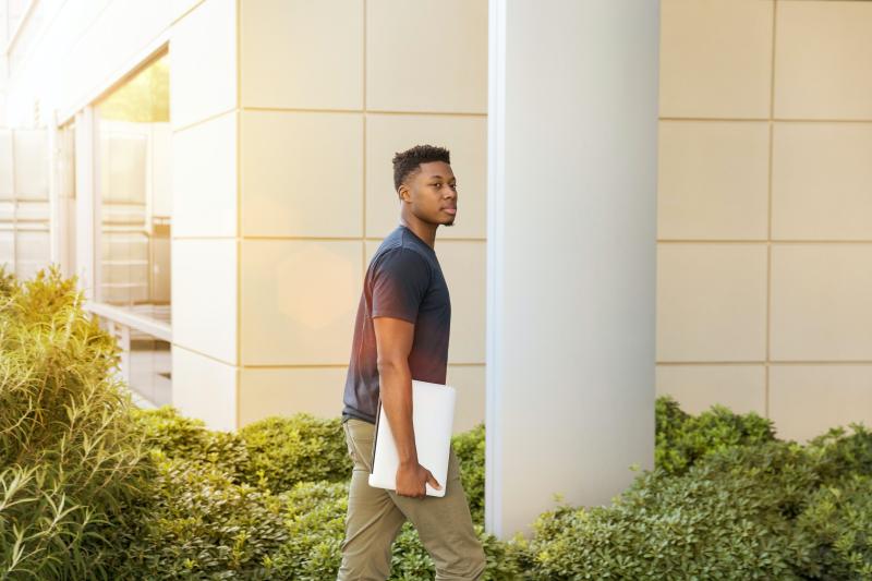 Photo of a young black man with a laptop walking into a building