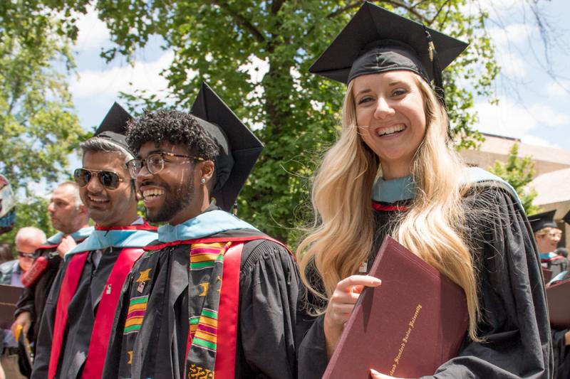 Photo of students in graduation robes with one holding her diploma.