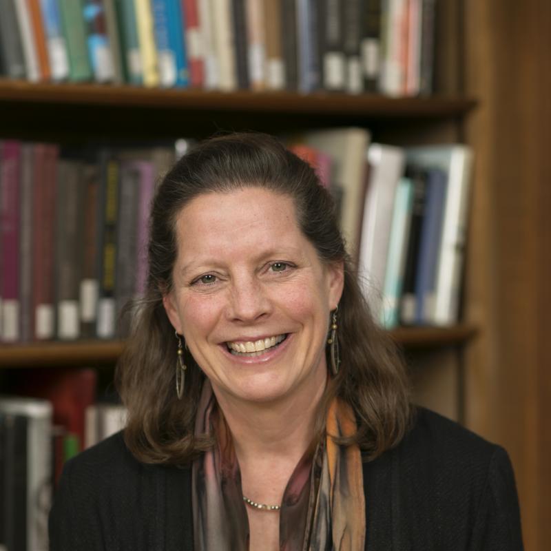 Photo of Alison Cook-Sather, smiling, standing in front of a library book shelf