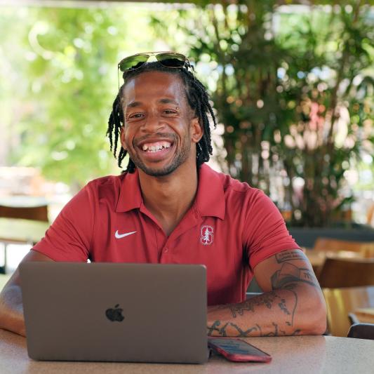 Photo of Jodi Anderson, Jr., smiling, in a cafe with his laptop