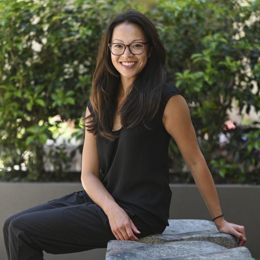 Thu Cung seated on a stone bench with lush greenery behind