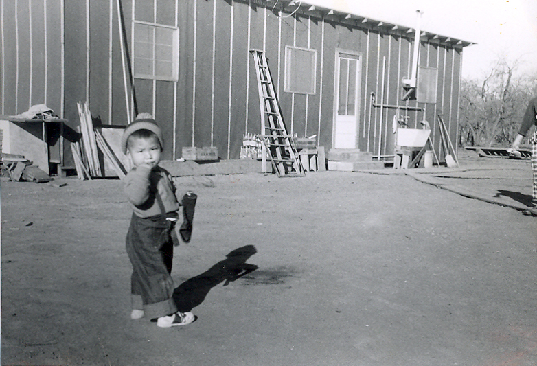 A small young boy in front of a shack.