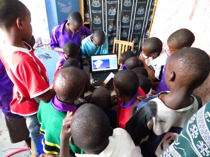 Students in Tanzania surrounding a laptop using TeachAIDS.