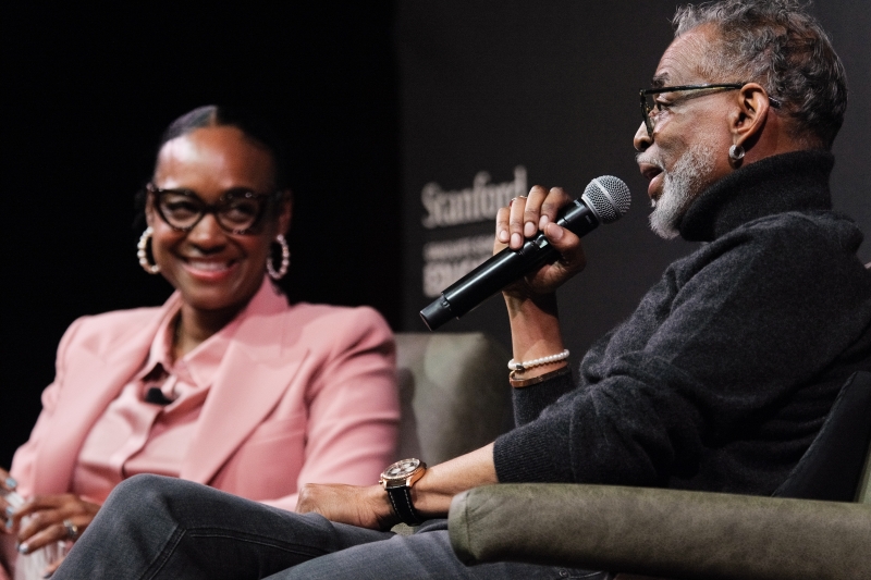 LeVar Burton holds a microphone and looks at Maisha Winn, who is smiling next to him.