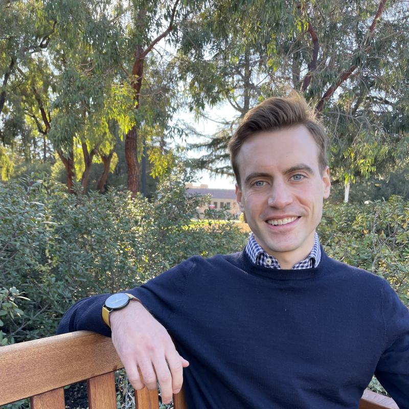 Ian Bott sitting outdoors on a bench on a sunlit afternoon