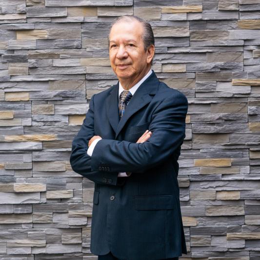 Marco Antonio Rodríguez Revoredo, arms folded, standing in front of a stone wall