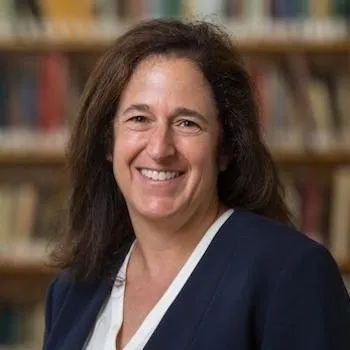 Picture of Susanna Loeb in white blouse and dark blazer in front of a wall of books.